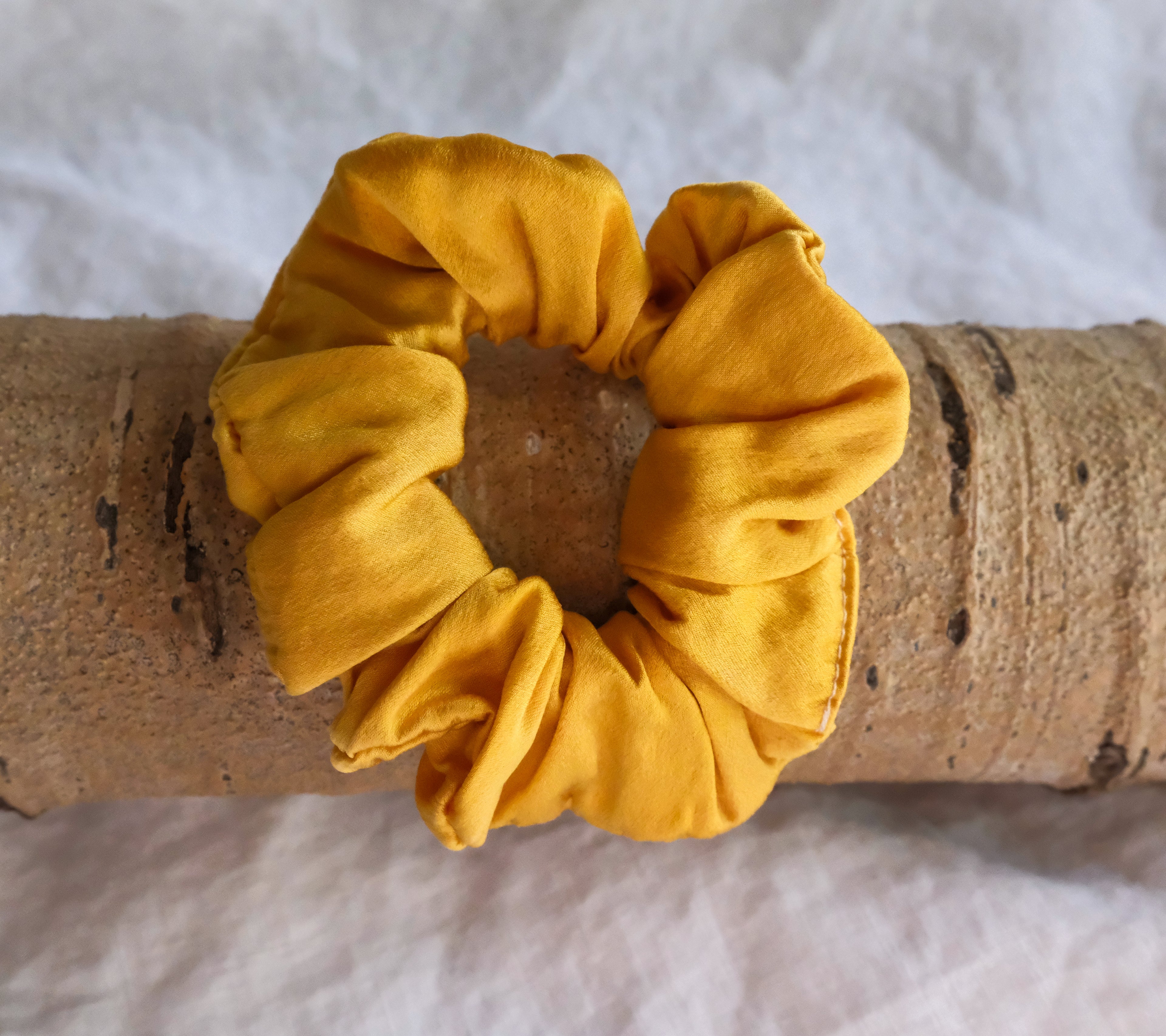 Golden scrunchie on a wooden log with a white background.