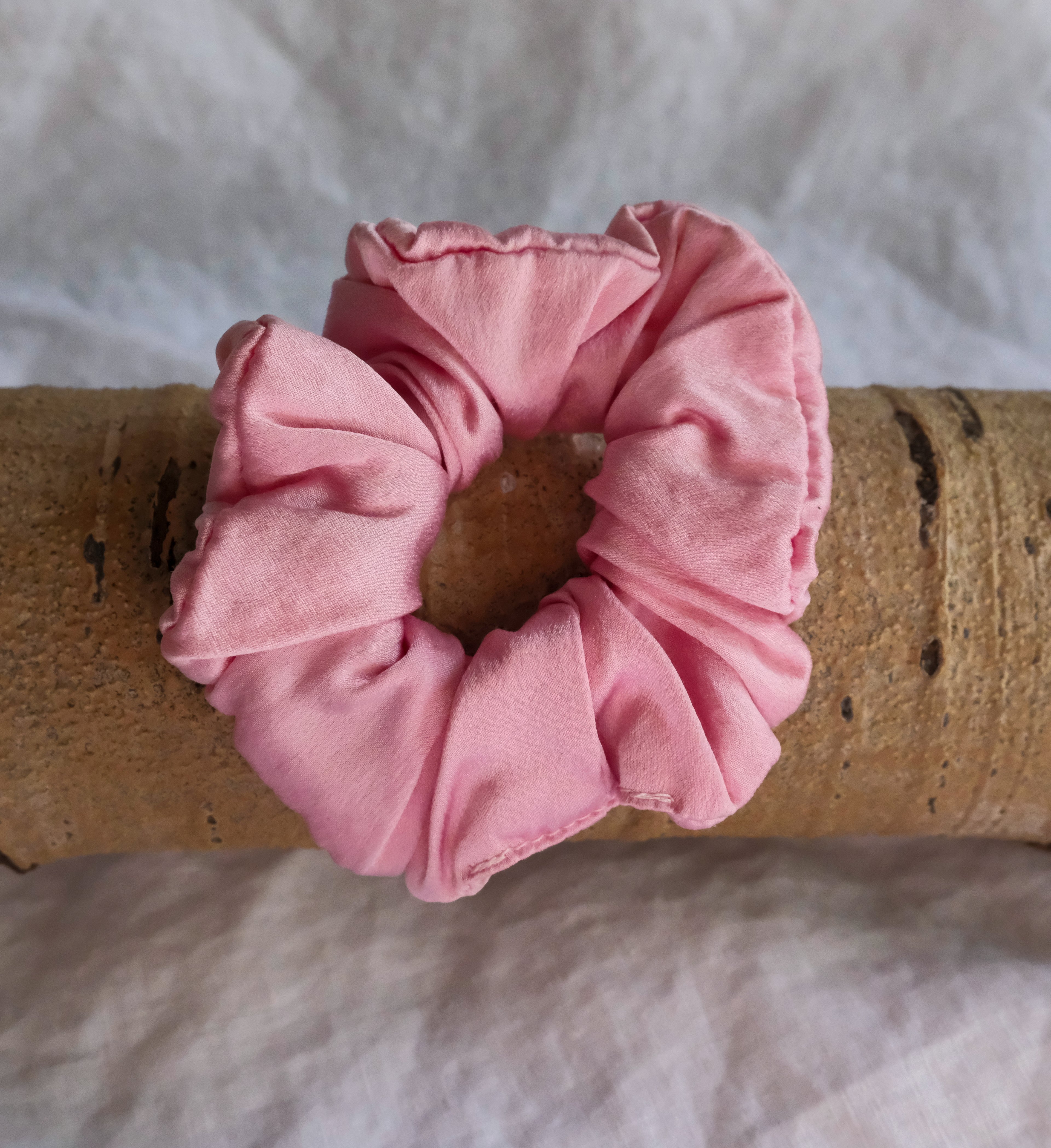 Pink scrunchie on a wooden stick with a white fabric background