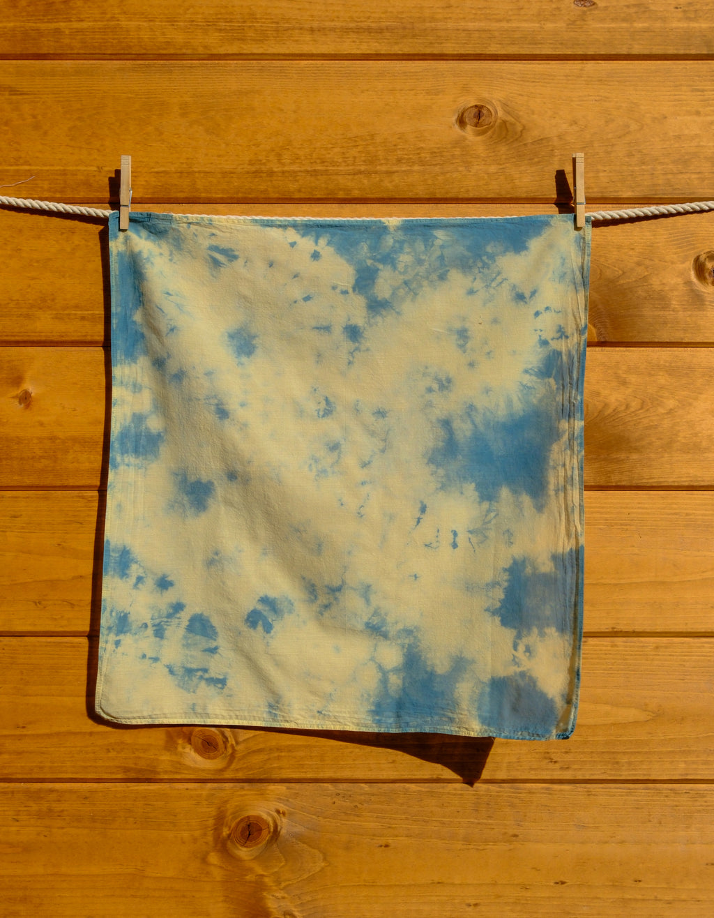Blue and yellow tie-dye bandana hanging on a wooden surface.