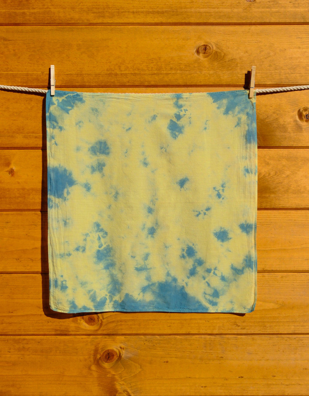 Blue and yellow tie-dye bandana hanging on a wooden surface.