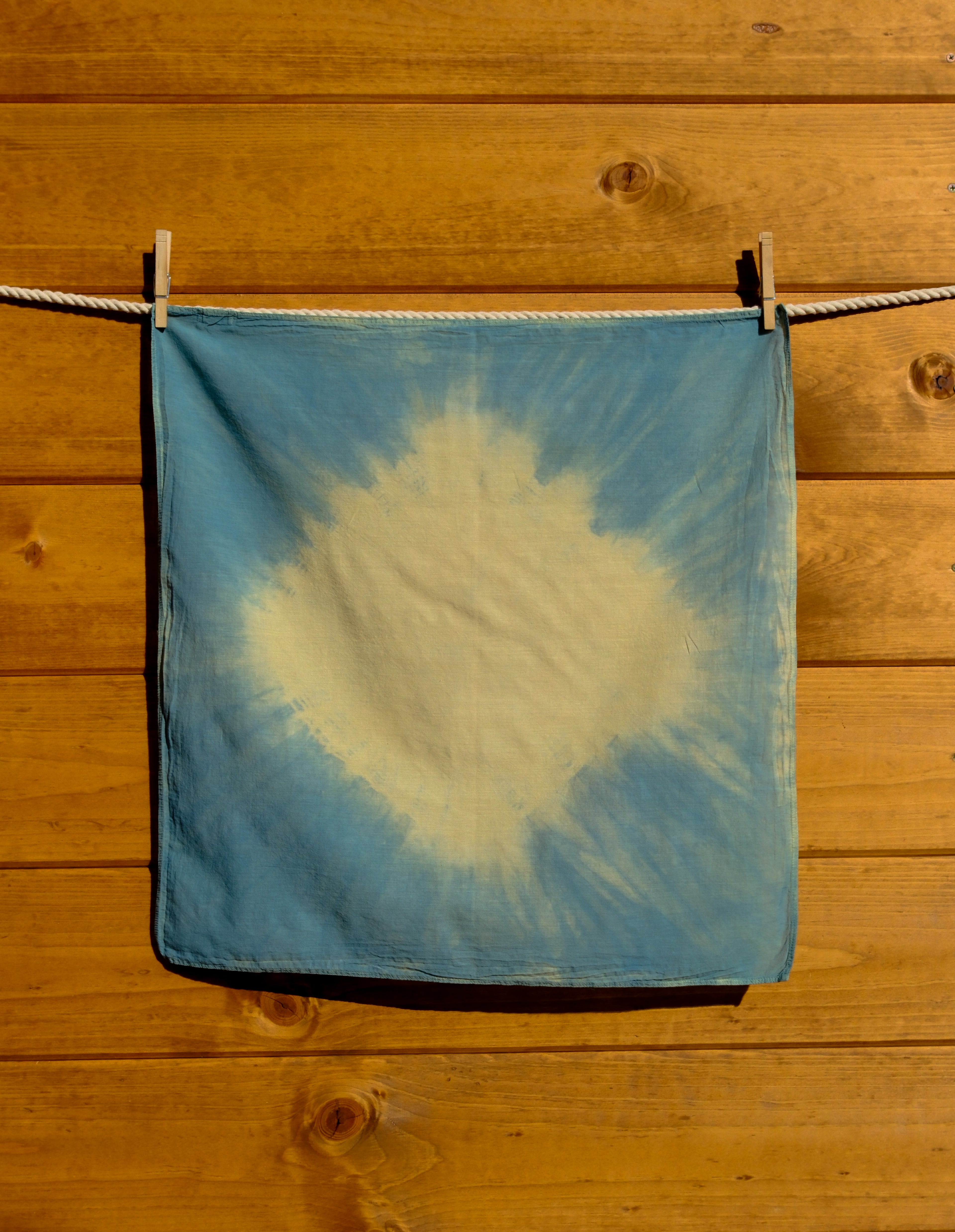 Blue and yellow sunburst tie-dye bandana hanging on a wooden surface.