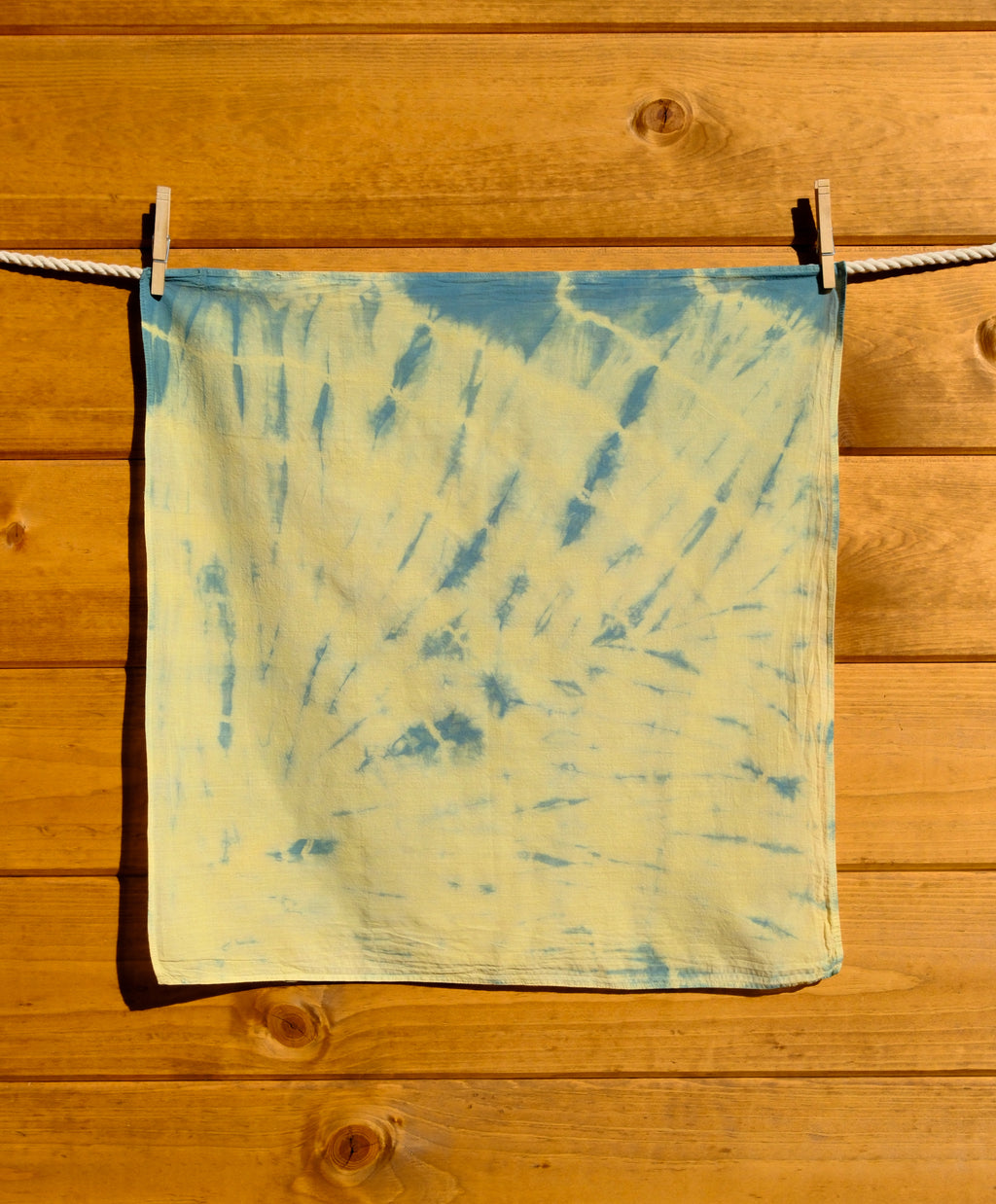 Blue and yellow tie-dye bandana hanging on a wooden surface.