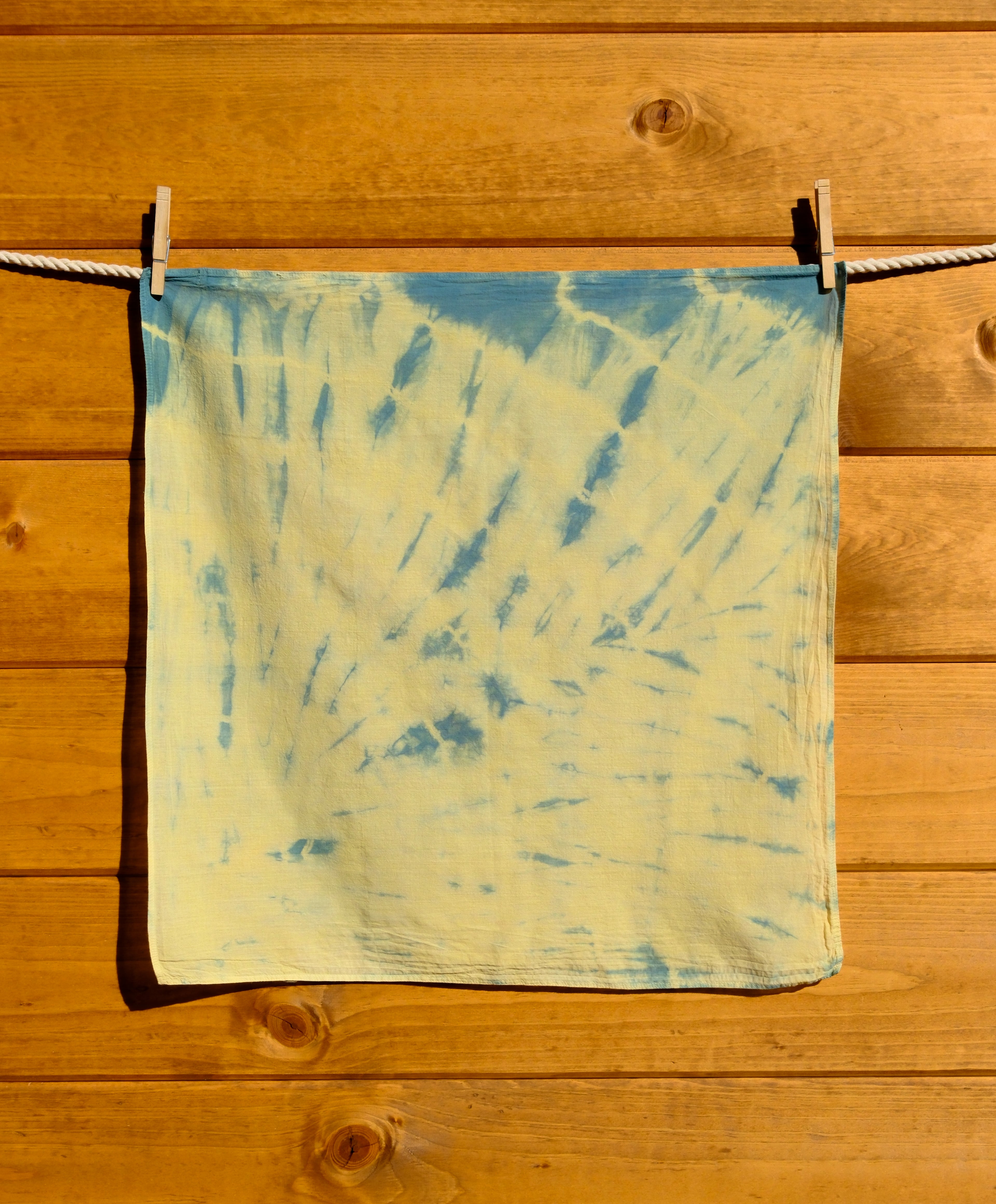 Blue and yellow tie-dye bandana hanging on a wooden surface.