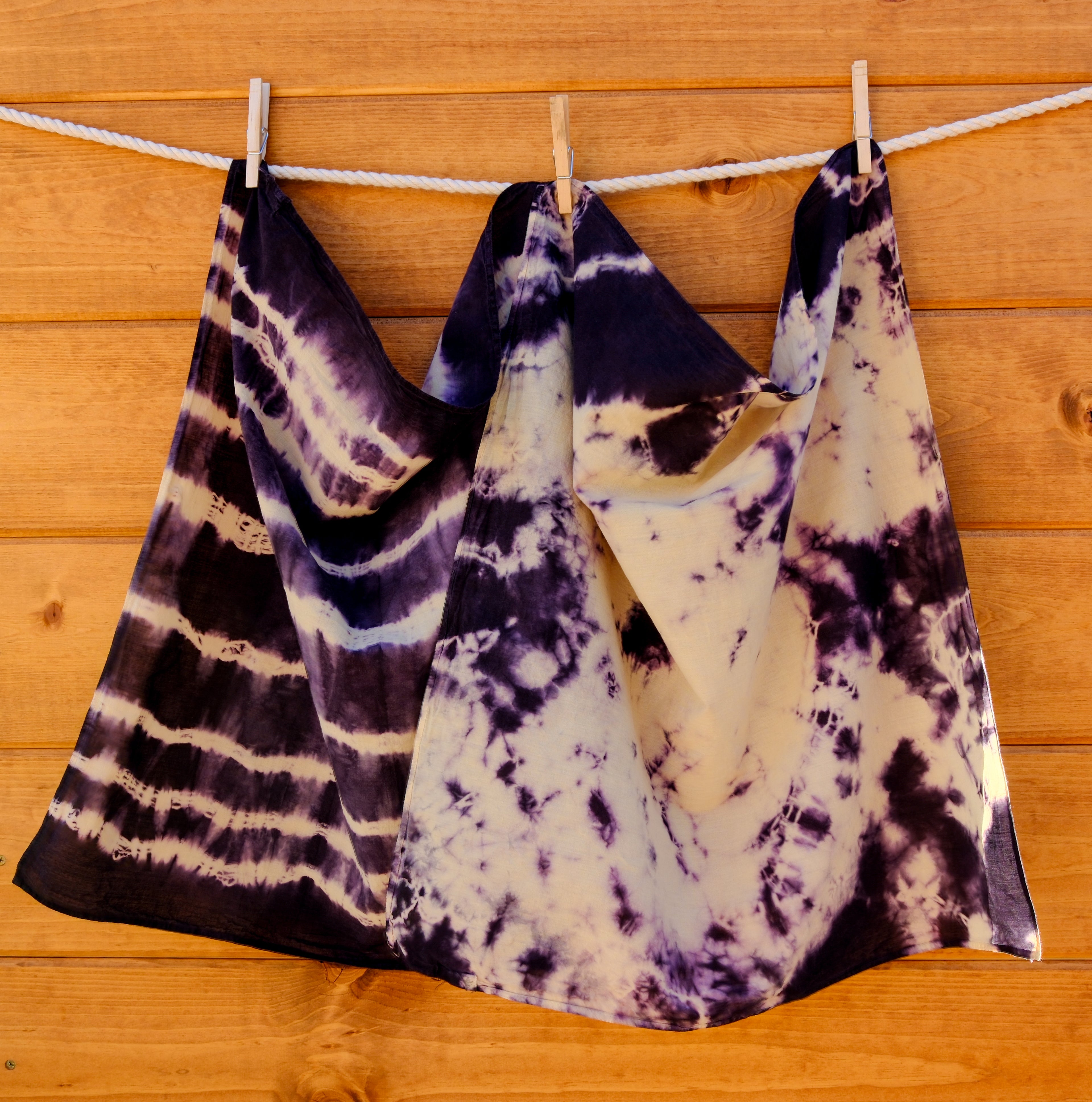 Tie-dye bandanas hanging on a clothesline against a wooden wall