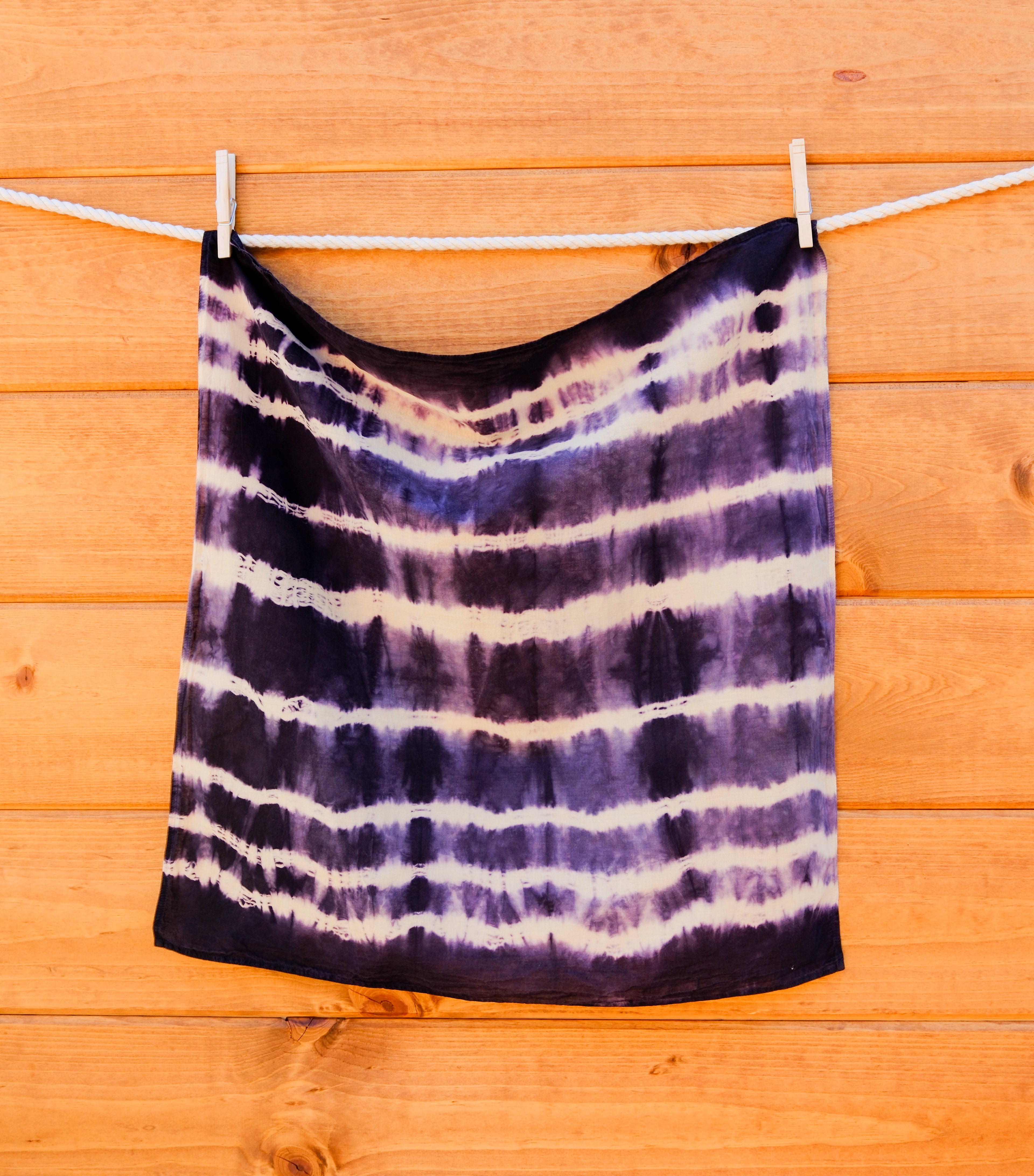 Tie-dye bandana hanging on a clothesline against a wooden wall