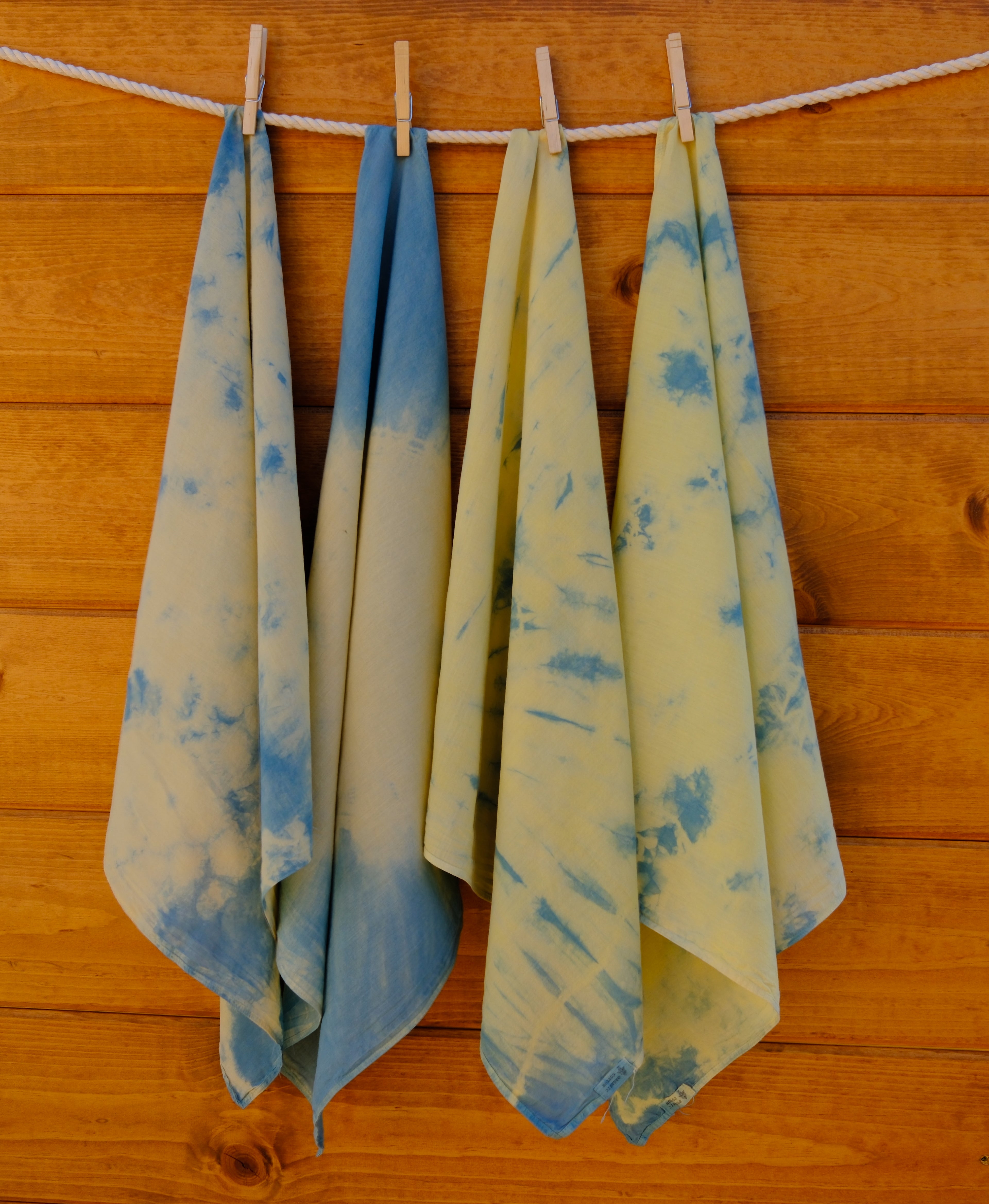Four bandanas with blue and yellow patterns hanging on a wooden wall.