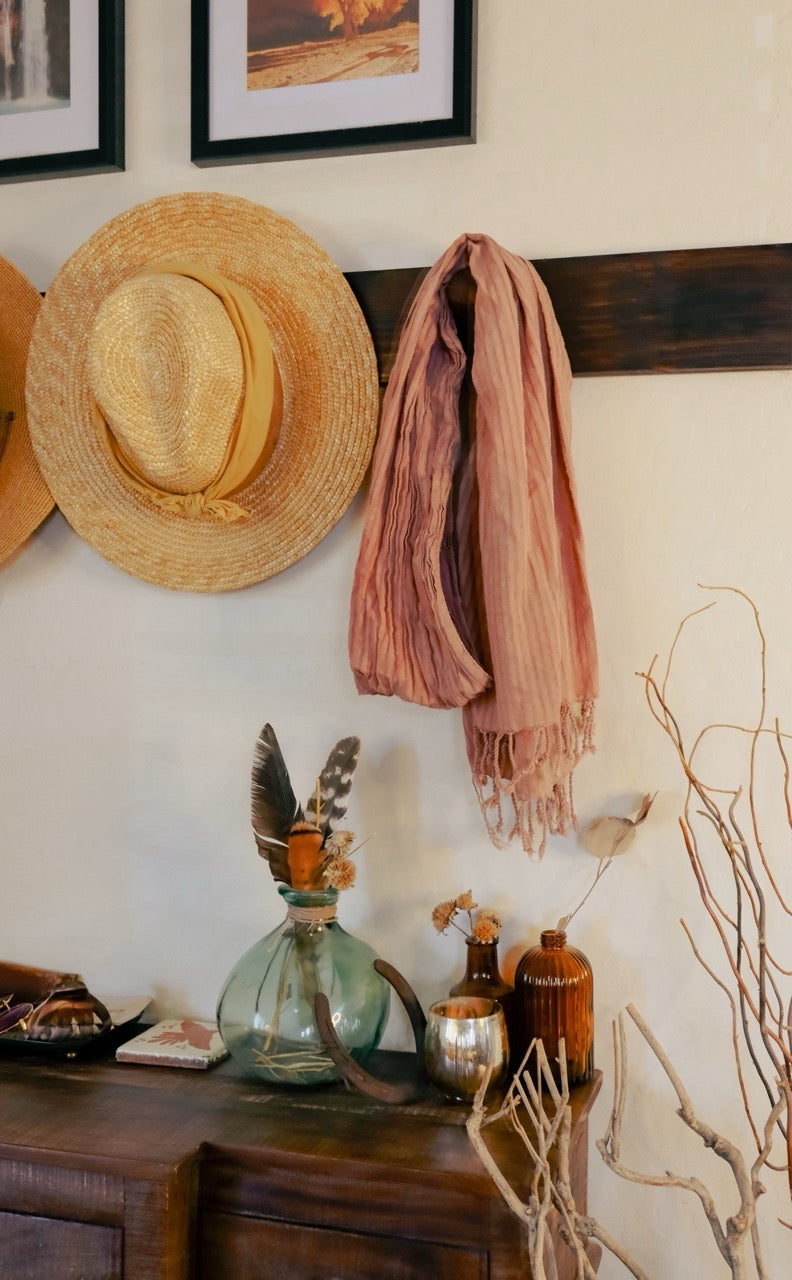 Decorative wall with hats, a scarf, vases, and a branch on a wooden surface.