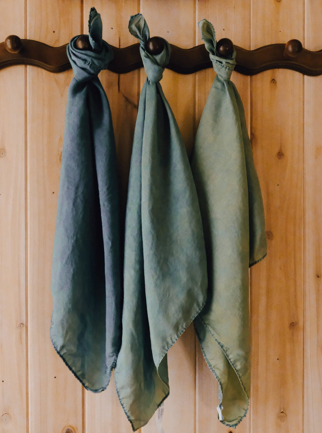 Three green-blue scarves hanging on a wooden wall with a rustic finish.