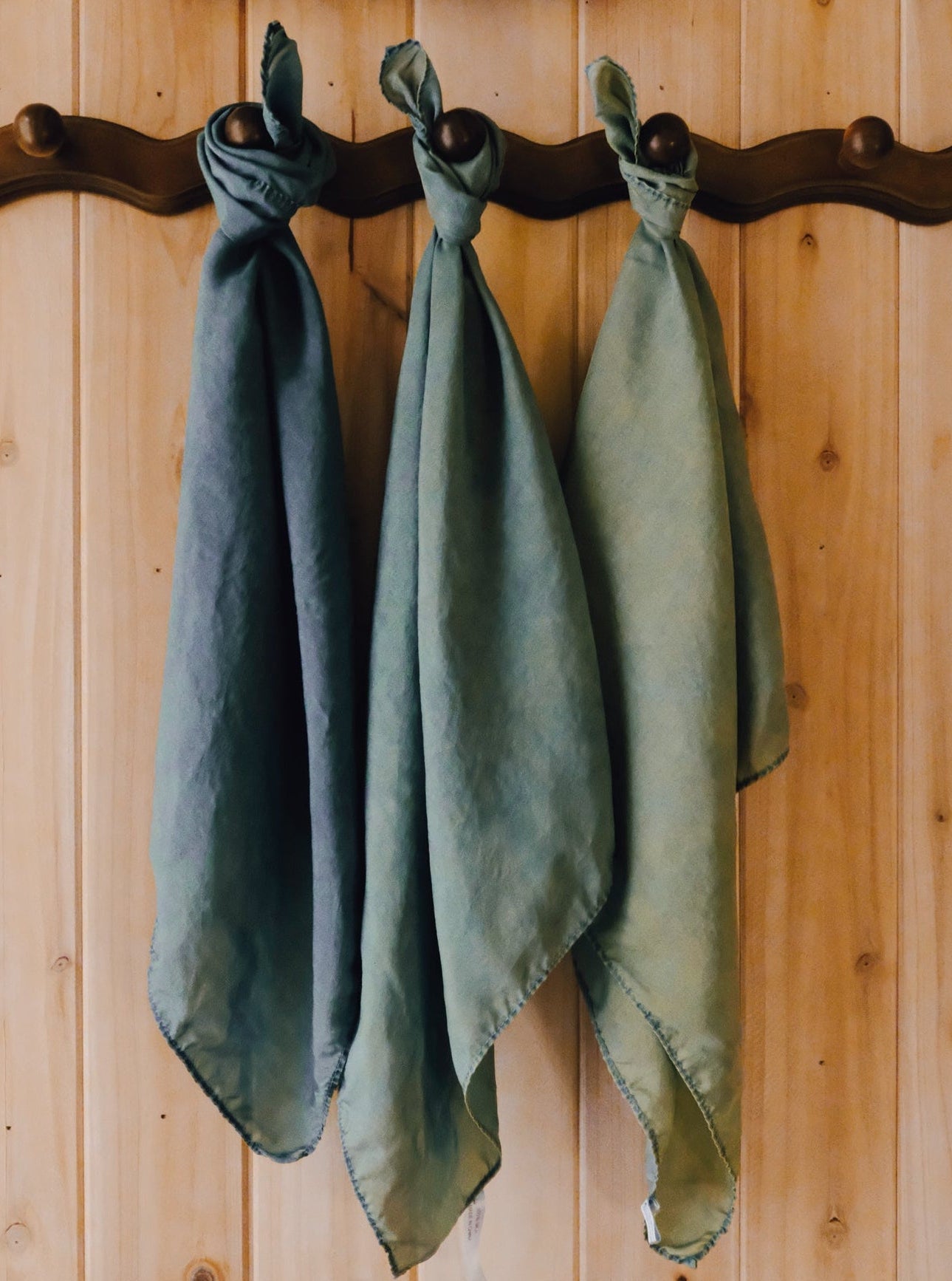 Three green-blue scarves hanging on a wooden wall with a rustic finish.