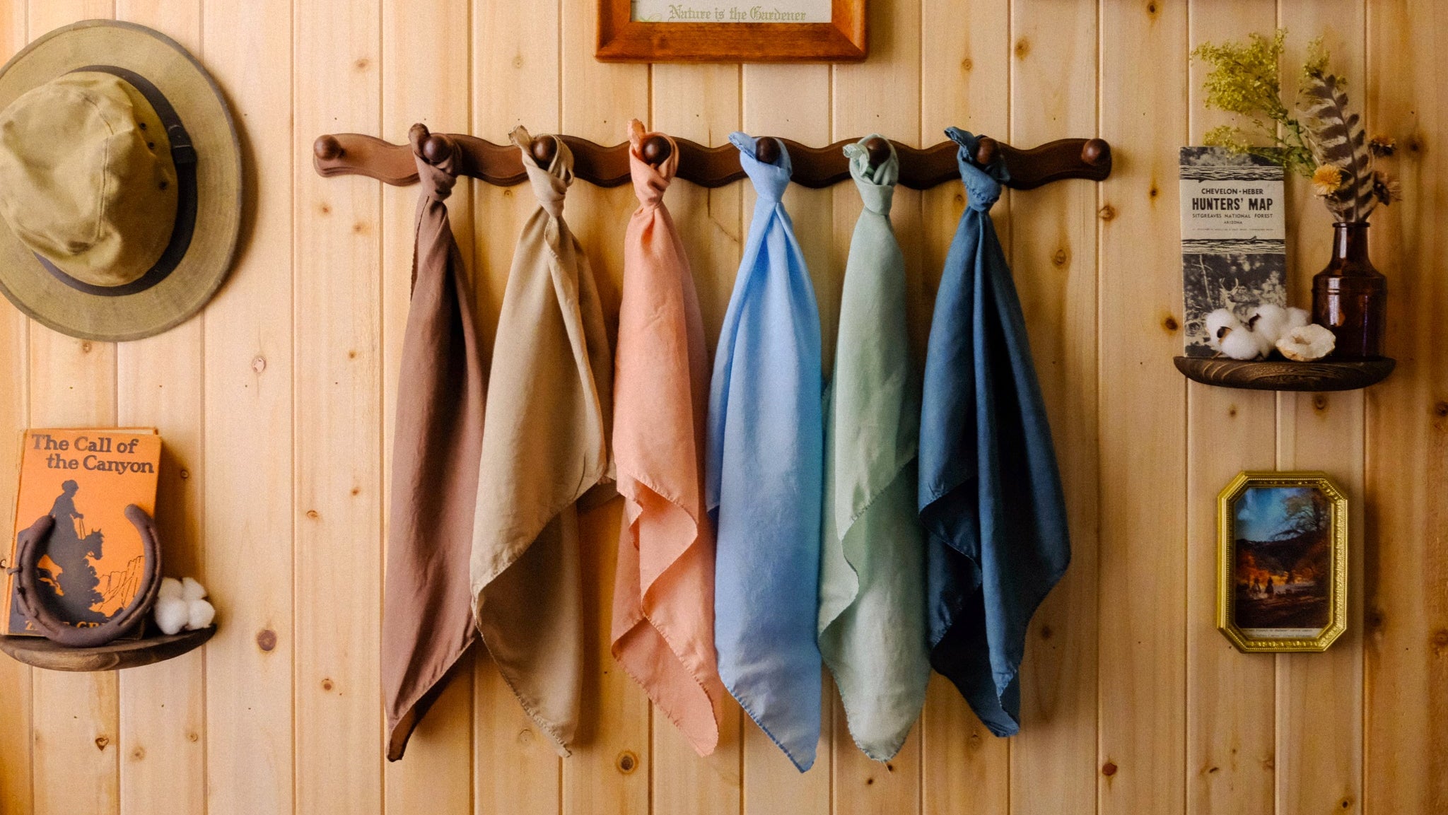 Colorful scarves hanging on a wooden wall with framed pictures and decor.