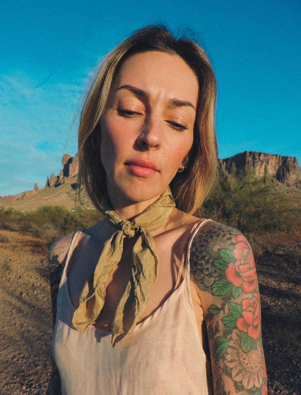 Woman with tattoos wearing a light green olive scarf in a desert landscape