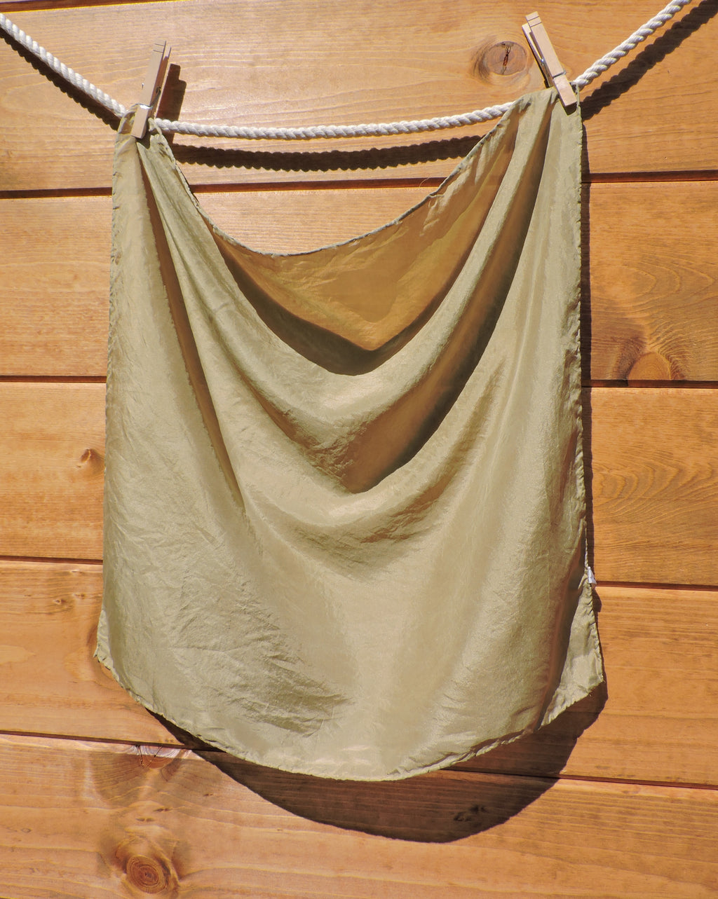 light Olive green scarf hanging on a clothesline against a wooden wall.