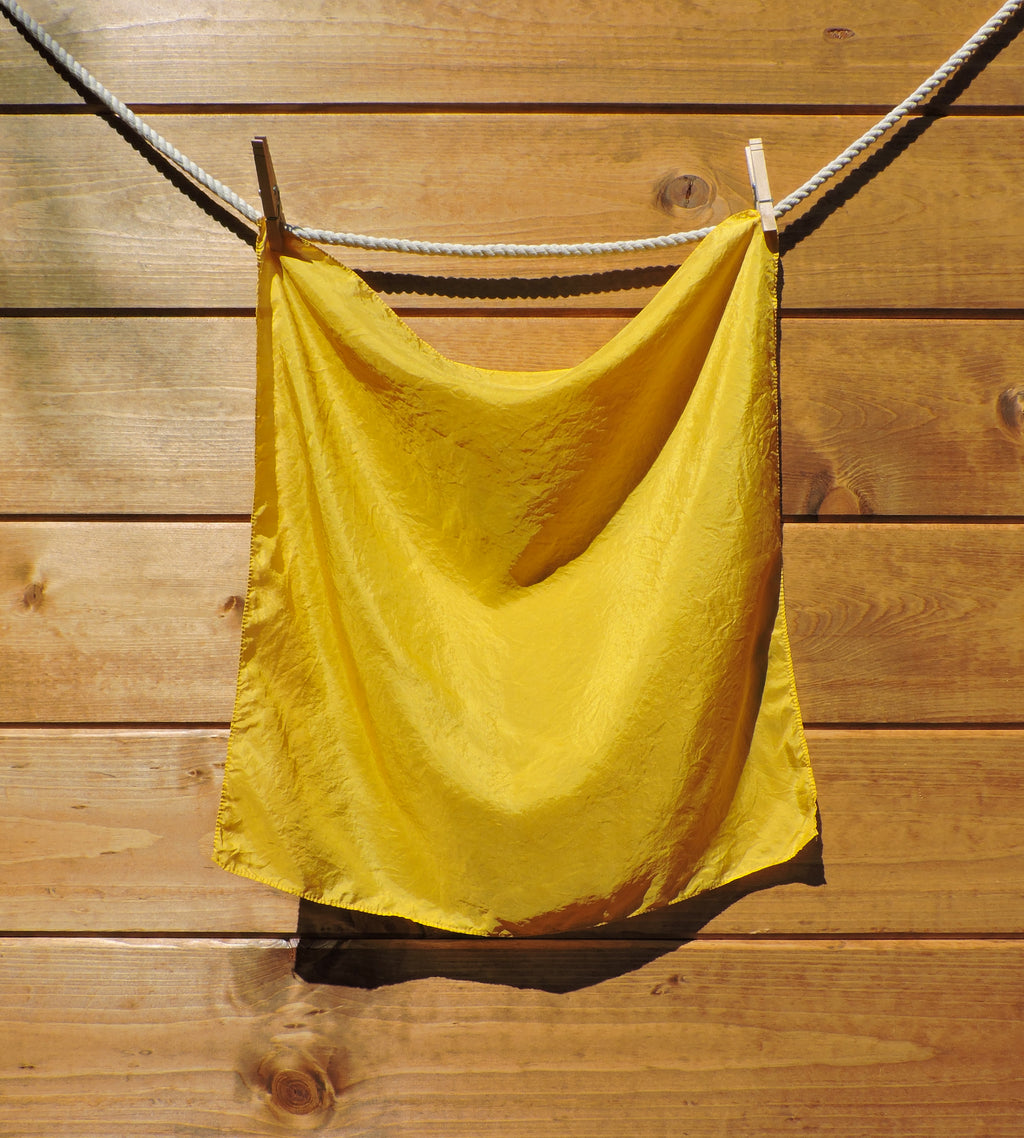 Bright yellow scarf hanging on a clothesline against a wooden wall