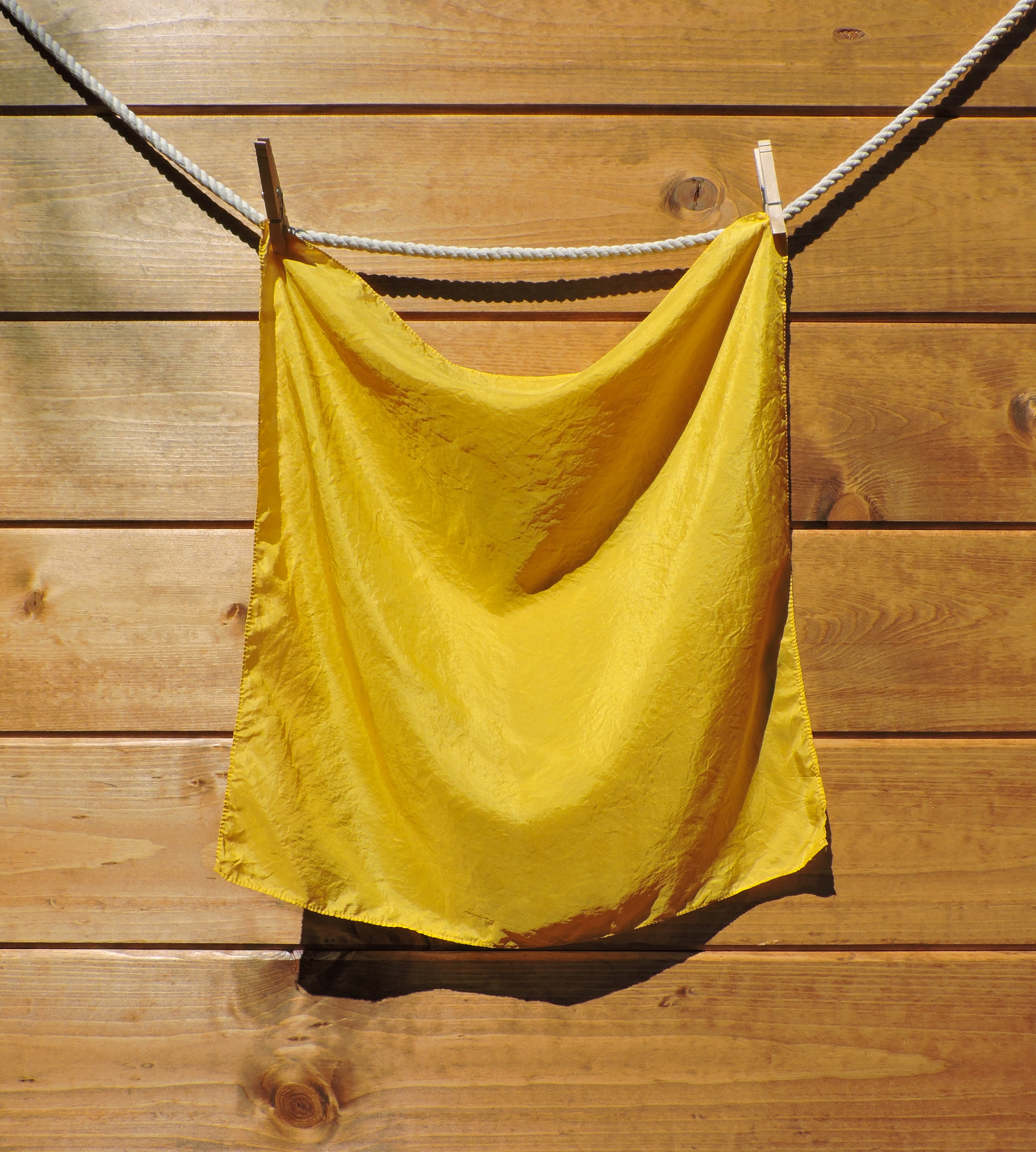 Bright yellow scarf hanging on a clothesline against a wooden wall