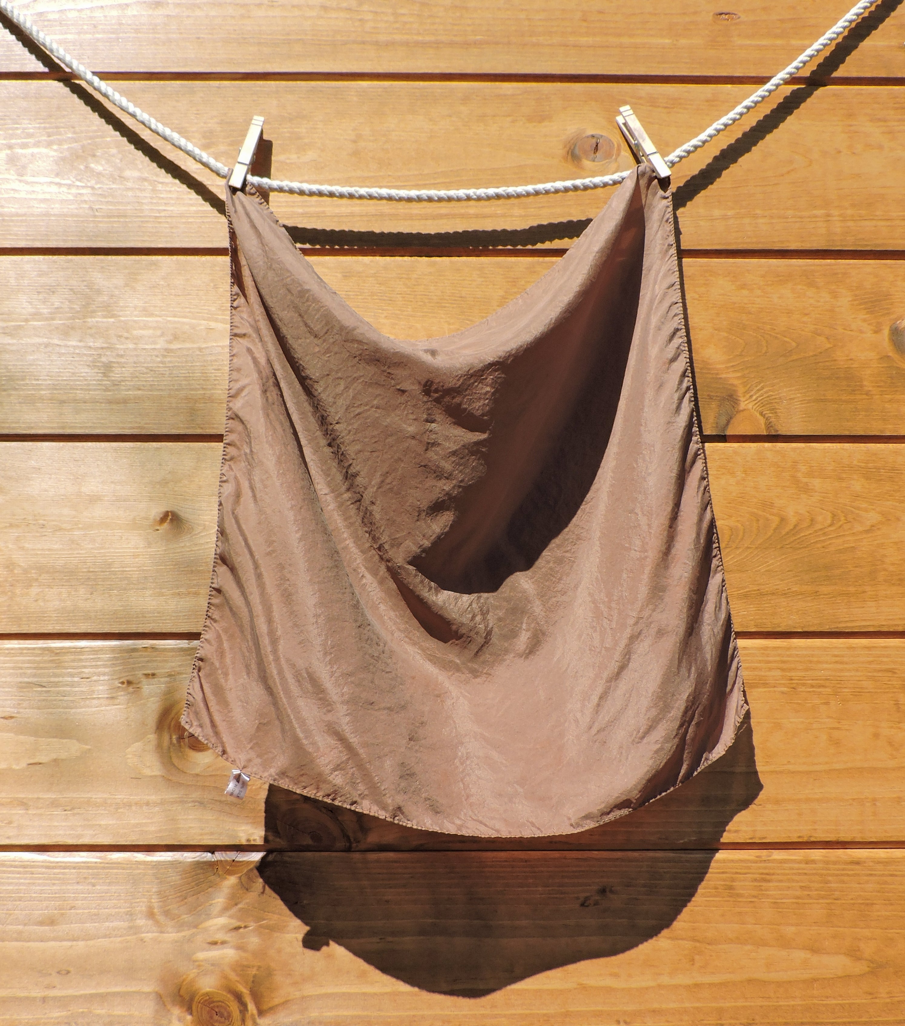 silk scarf hanging on a clothesline against a wooden wall