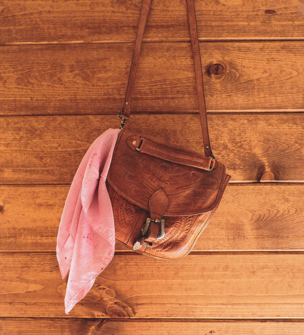 Brown leather bag with a pink scarf on a wooden surface