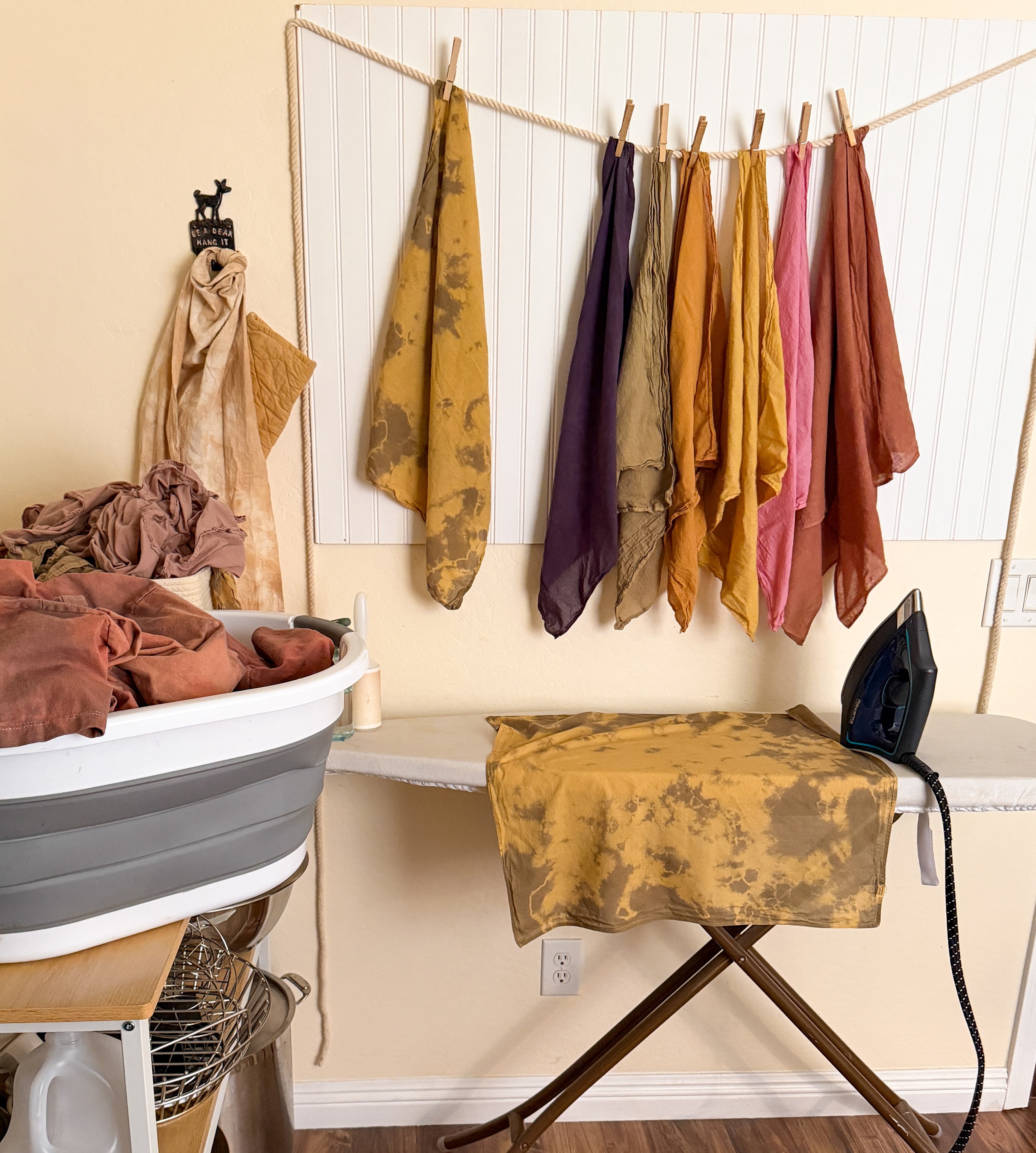 Laundry room with clothes hanging on a line, ironing board, and washing machine.
