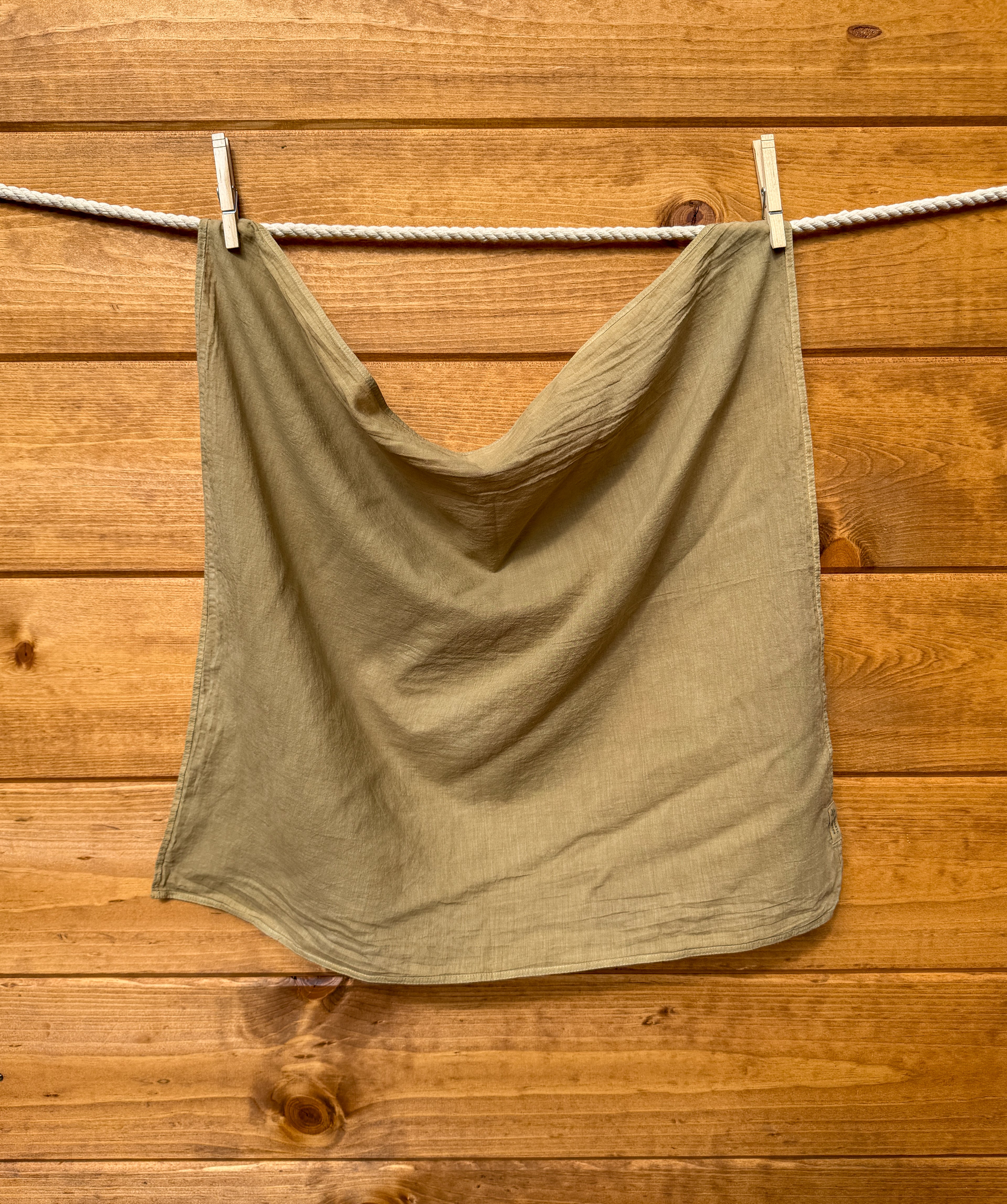 olive green bandana hanging on a clothesline against a wooden wall