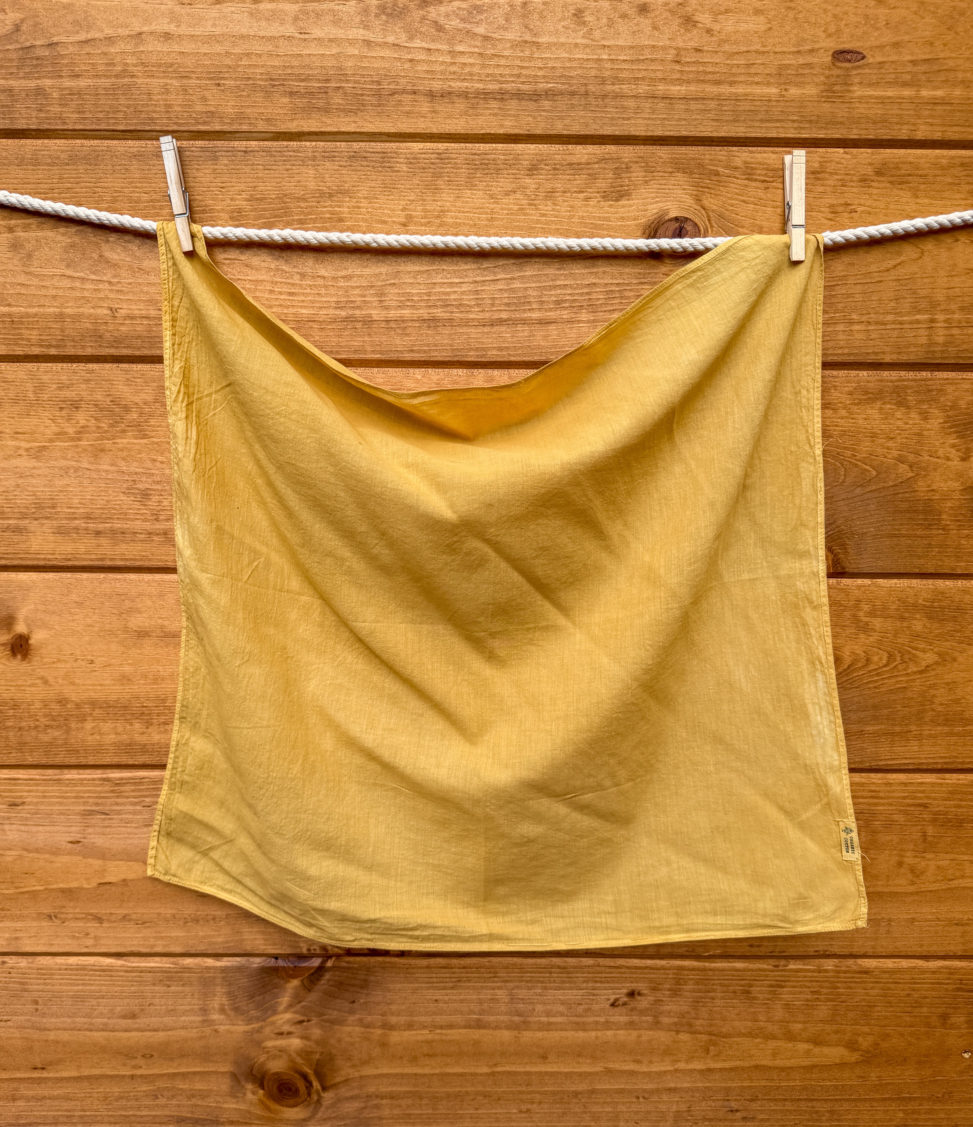 Yellow bandana hanging on a clothesline against a wooden wall