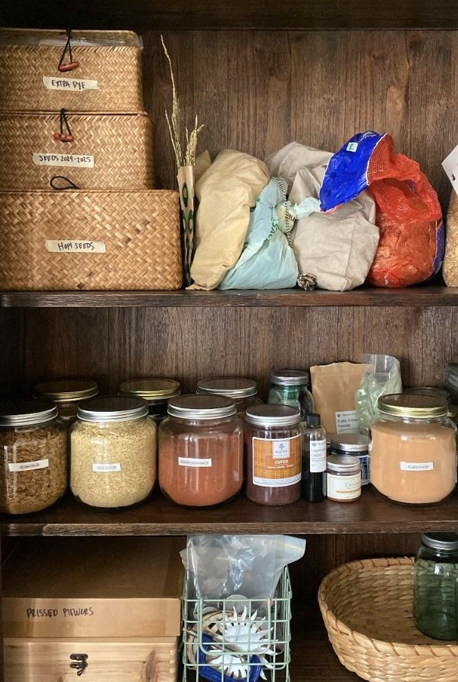 Shelves with jars, bags, and baskets in a cabinet filled with natural dyes.