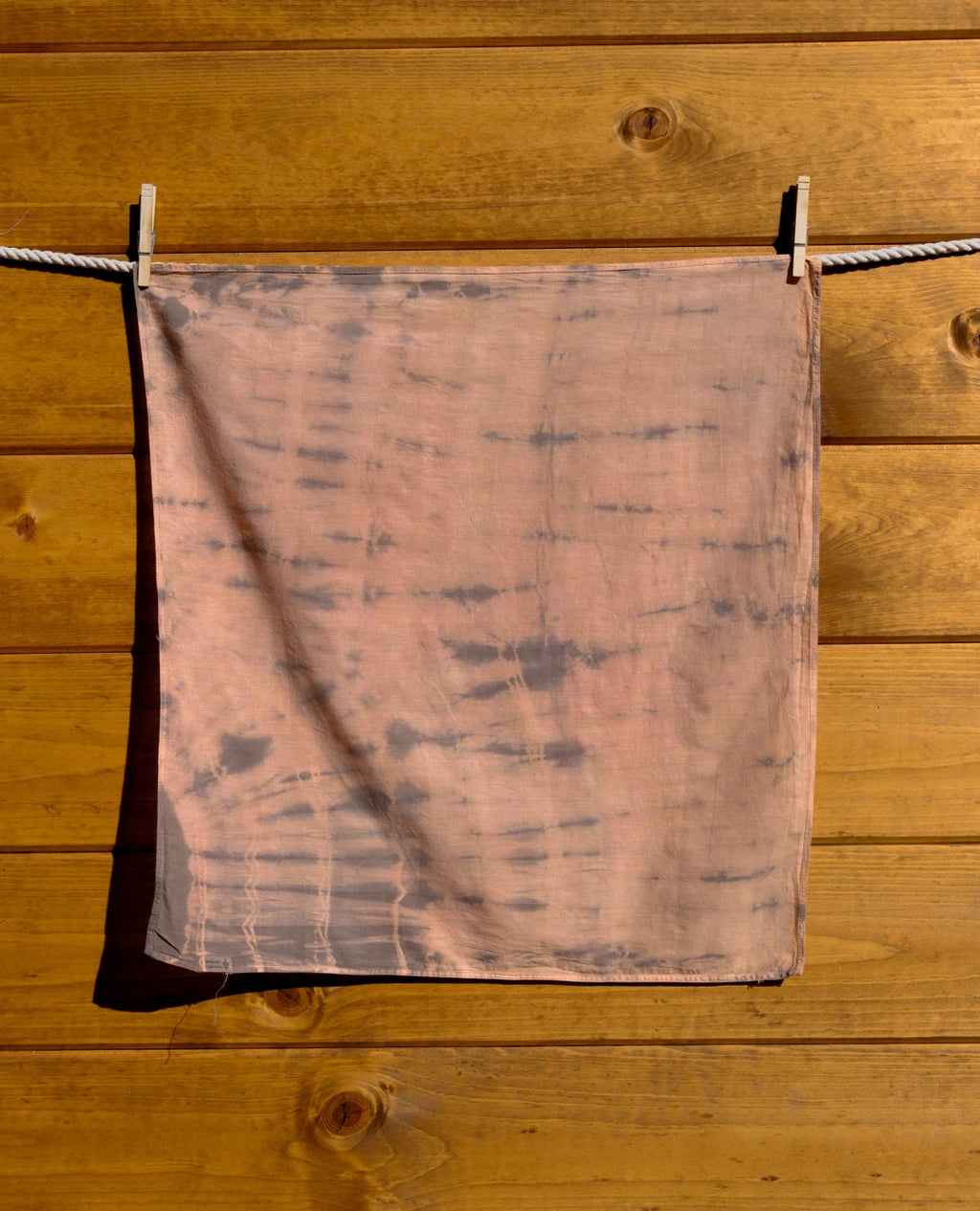 tie-dye bandana hanging on a clothesline against a wooden wall