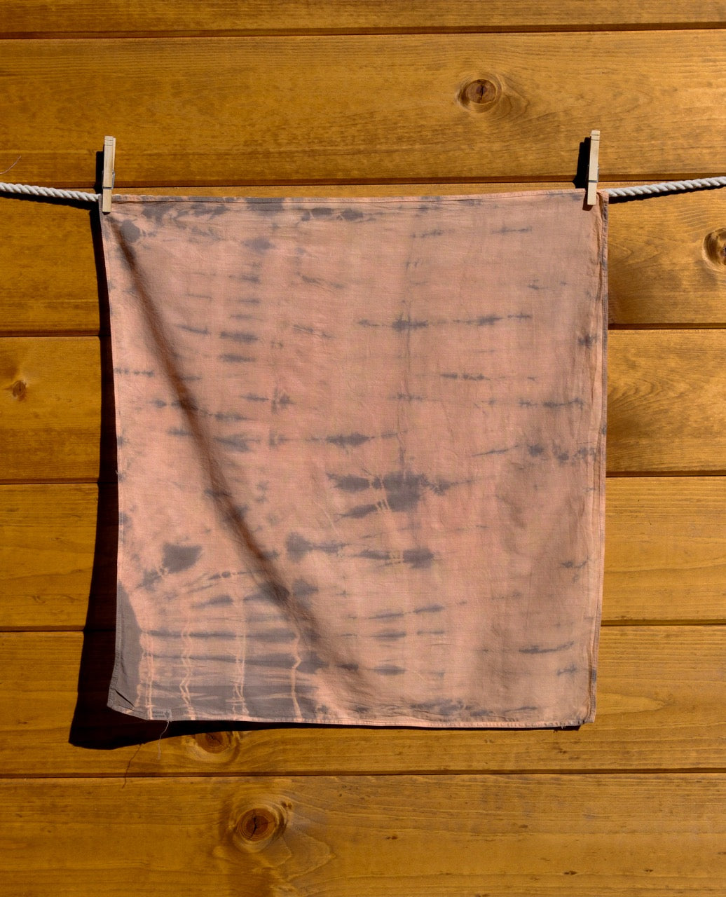 tie-dye bandana hanging on a clothesline against a wooden wall